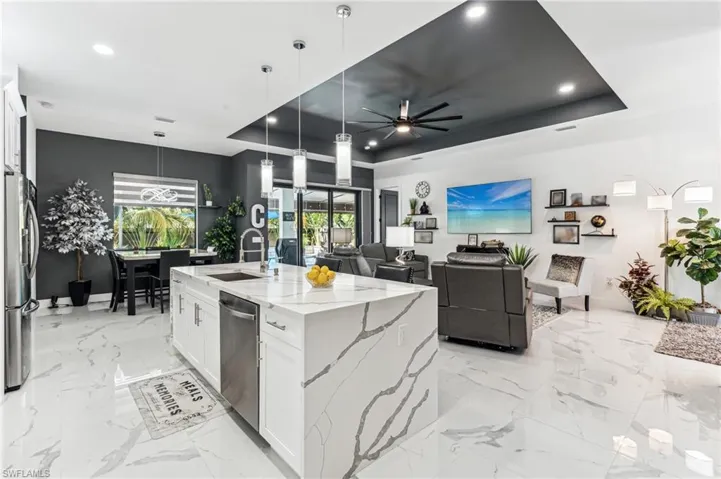 Kitchen featuring white cabinetry, a tray ceiling, stainless steel appliances, a sink, and light stone countertops