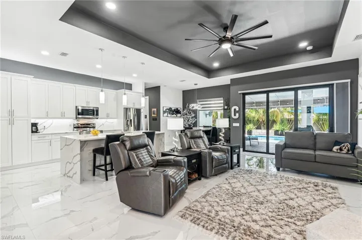 Living room with marble finish floor, a ceiling fan, a tray ceiling, and visible vents