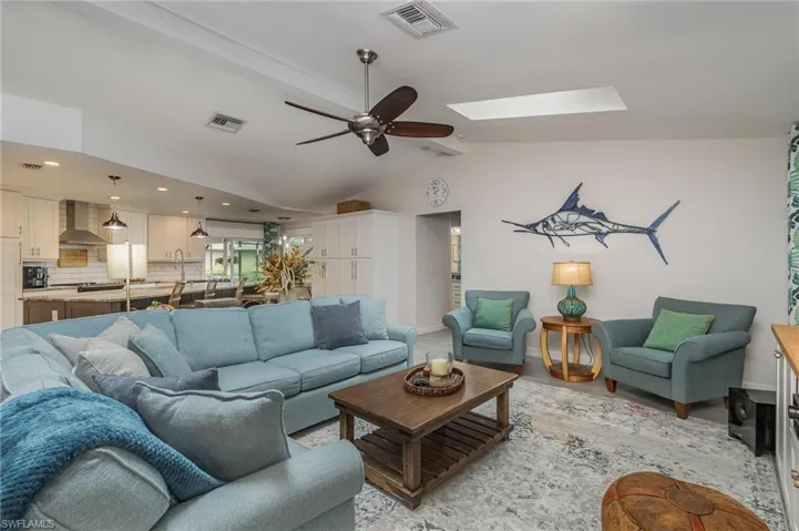 Living room with lofted ceiling with skylight, light plank style flooring, and ceiling fan