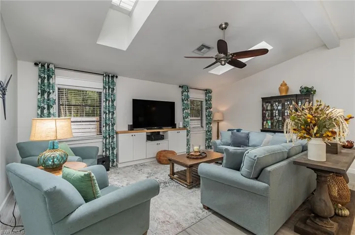 Living room featuring lofted ceiling with skylight, light hardwood / plank style flooring, and ceiling fan