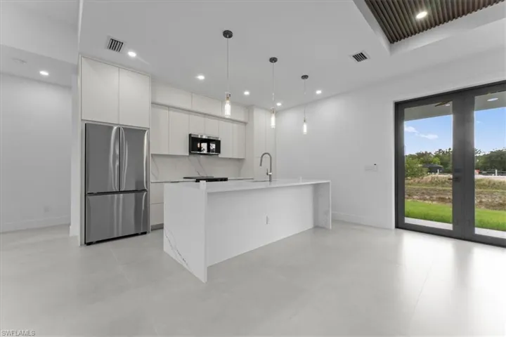 Kitchen featuring stainless steel appliances, decorative light fixtures, modern cabinets, an island with sink, and white cabinets