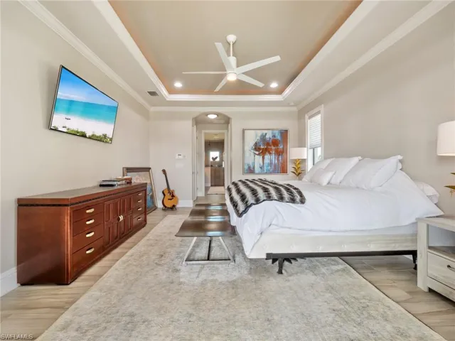 Bedroom with a tray ceiling, arched walkways, crown molding, visible vents, and light wood-type flooring