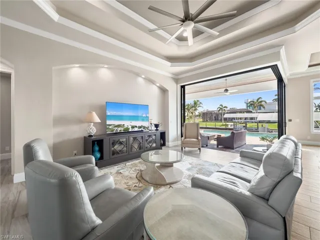 Living area featuring a tray ceiling, crown molding, a ceiling fan, a sunroom, and baseboards