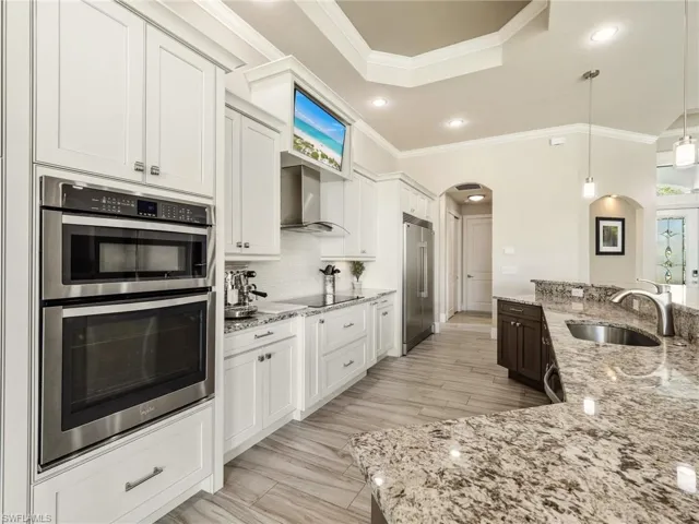 Kitchen featuring arched walkways, appliances with stainless steel finishes, white cabinets, a sink, and wall chimney range hood