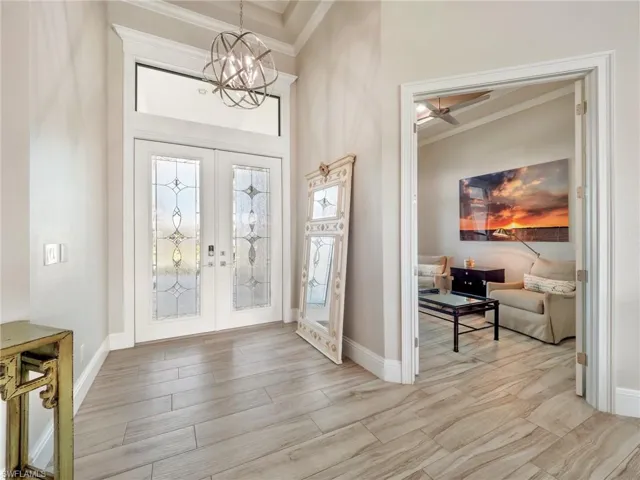 Entryway featuring baseboards, light wood-style flooring, ornamental molding, an inviting chandelier, and french doors