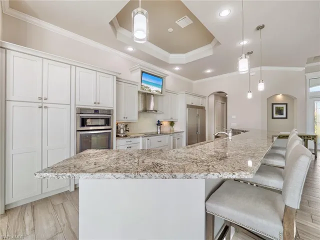 Kitchen featuring arched walkways, a large island, white cabinets, and stainless steel built in fridge
