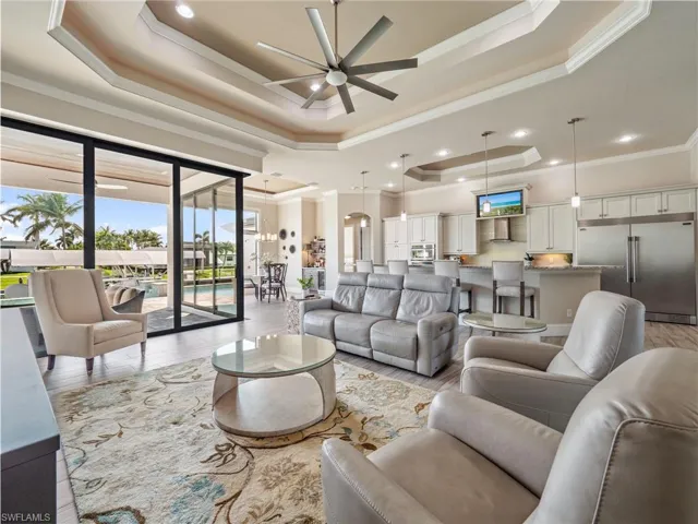 Living area with light wood-type flooring, crown molding, a tray ceiling, and a ceiling fan