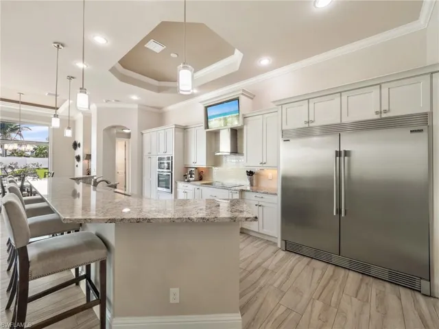 Kitchen with light stone counters, stainless steel appliances, white cabinetry, wall chimney exhaust hood, and decorative light fixtures