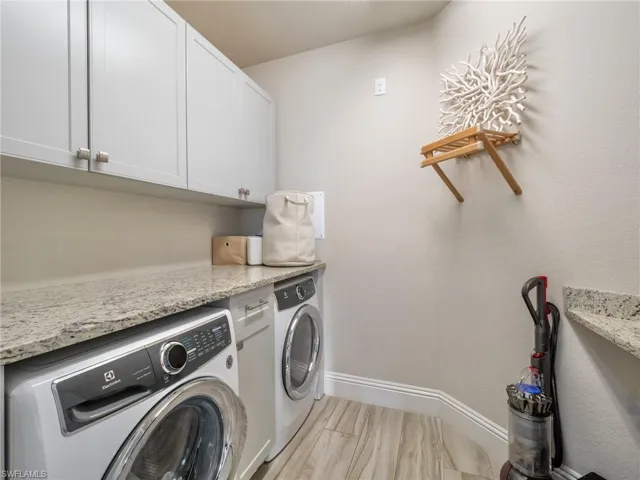 Laundry area featuring washing machine and dryer, cabinet space, and baseboards