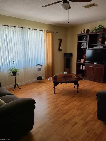 Living room with light wood-style flooring, a ceiling fan, baseboards, and a textured ceiling