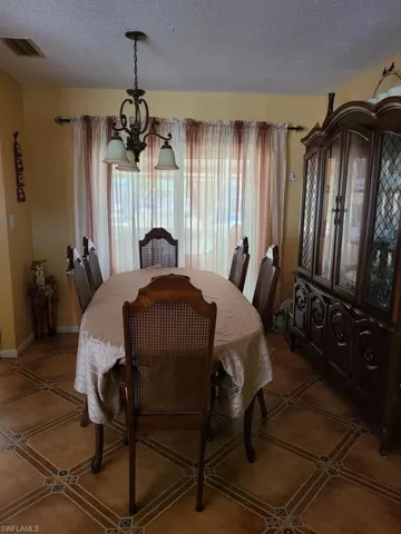 Dining room with a textured ceiling, a chandelier, light tile patterned flooring, and baseboards