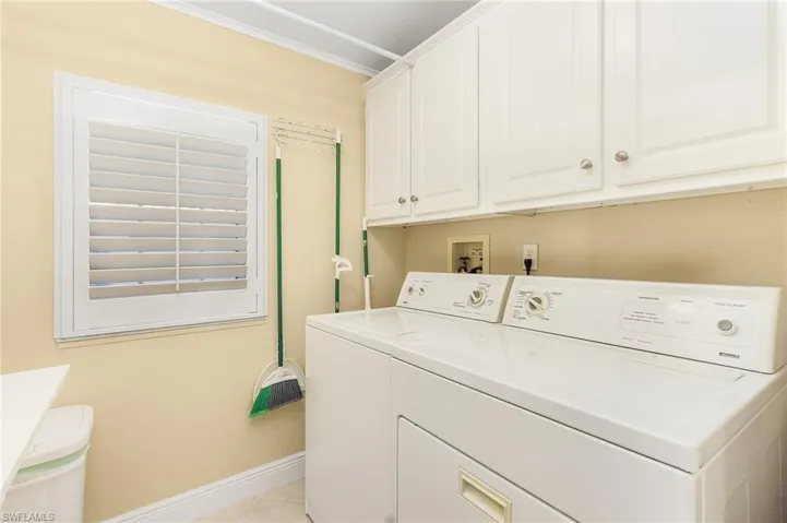 Washroom with cabinet space, light tile patterned flooring, baseboards, ornamental molding, and washer and clothes dryer