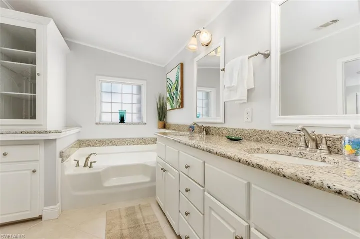 Bathroom featuring a garden tub, visible vents, a sink, tile patterned floors, and ornamental molding
