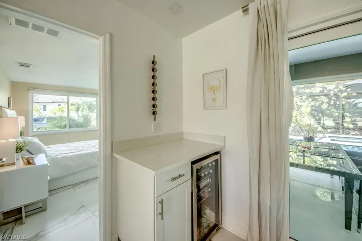 Bar with wine cooler, white cabinetry, and light stone counters