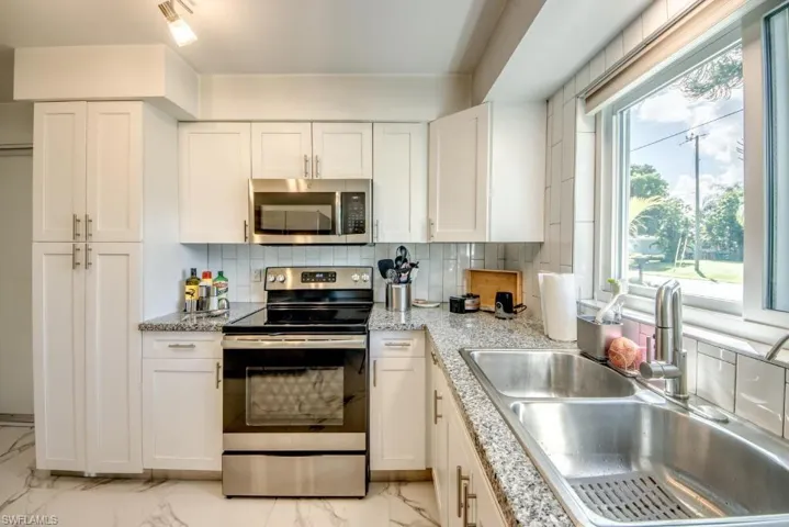 Kitchen with stainless steel appliances, white cabinetry, tasteful backsplash, light stone counters, and light marble finish floors