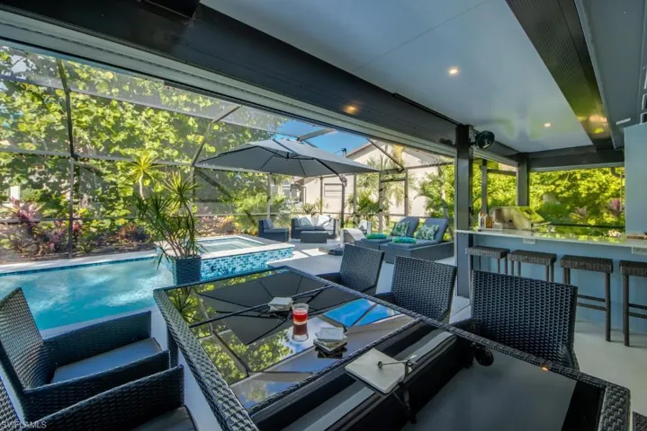 View of patio / terrace featuring a sunroom, an outdoor bar and dining area, a pool with connected hot tub, glass enclosure, and an outdoor kitchen