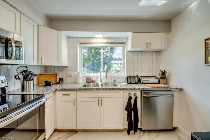 Kitchen featuring stainless steel appliances, decorative backsplash, white cabinets, and light stone counters
