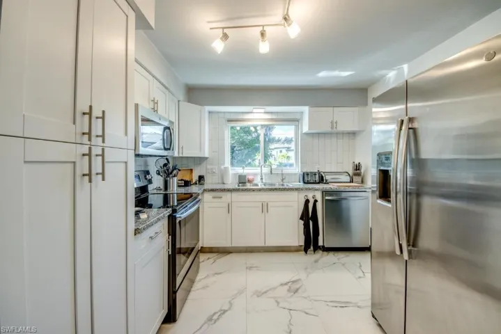 Kitchen with stainless steel appliances, white cabinetry, light marble finish flooring, light stone counters, and decorative backsplash