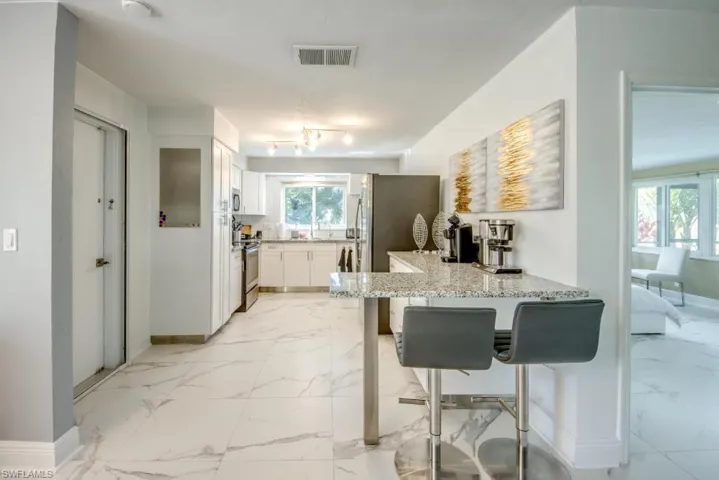 Kitchen featuring a breakfast bar area, light marble finish flooring, a peninsula, white cabinets, and light stone counters