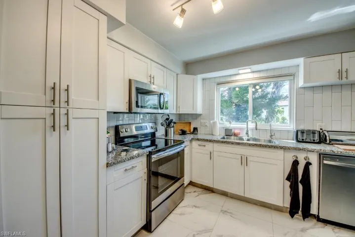 Kitchen with stainless steel appliances, tasteful backsplash, white cabinets, and light stone countertops