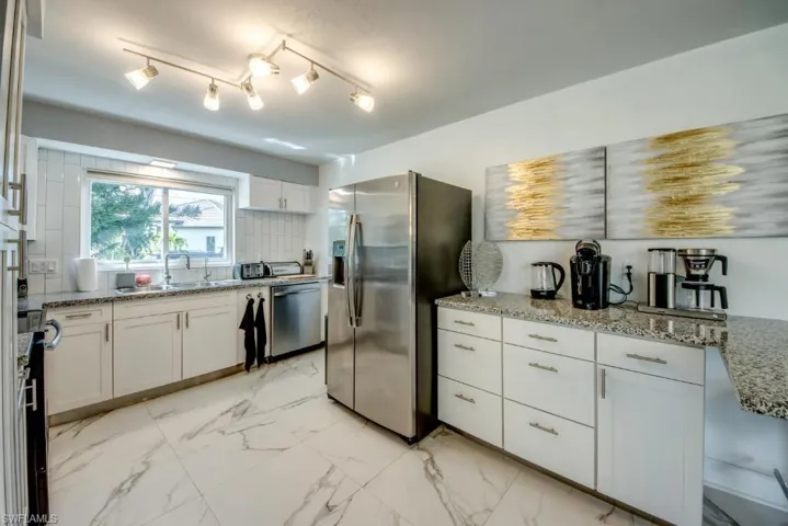 Kitchen featuring light stone counters, stainless steel appliances, white cabinetry, light marble finish flooring, and tasteful backsplash