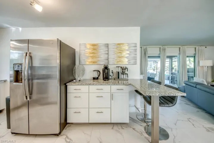 Kitchen featuring a breakfast bar area, stainless steel refrigerator with ice dispenser, white cabinetry, light stone counters, and light marble finish floors