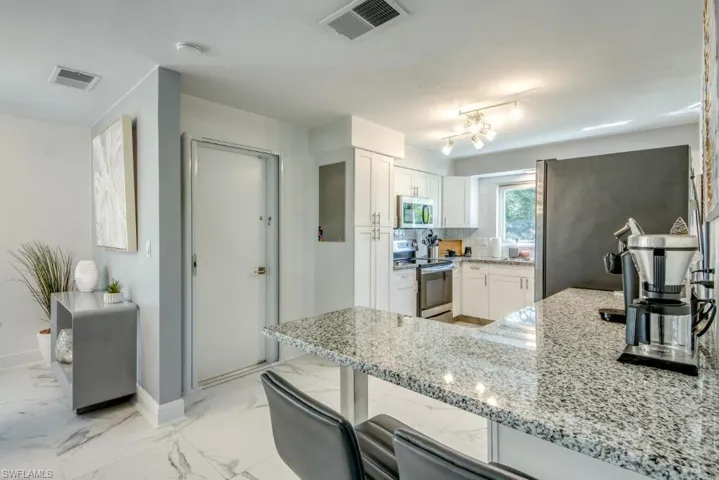 Kitchen with stainless steel appliances, light stone countertops, white cabinetry, a peninsula, and light marble finish flooring