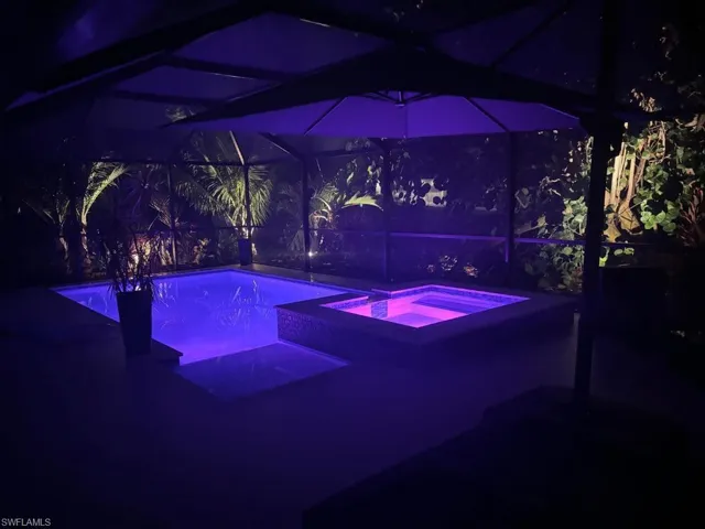 Pool at night featuring a lanai and a pool with connected hot tub