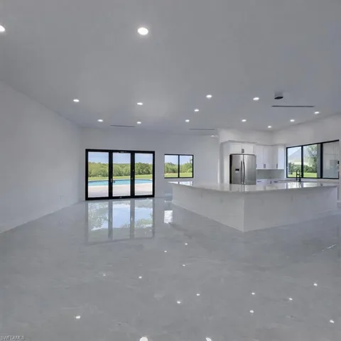 Kitchen with white cabinets, open floor plan, stainless steel fridge with ice dispenser, light stone counters, and a large island