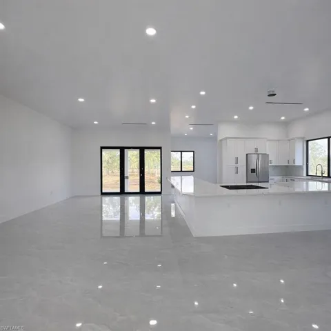 Kitchen with white cabinetry, open floor plan, recessed lighting, light stone countertops, and stainless steel fridge with ice dispenser