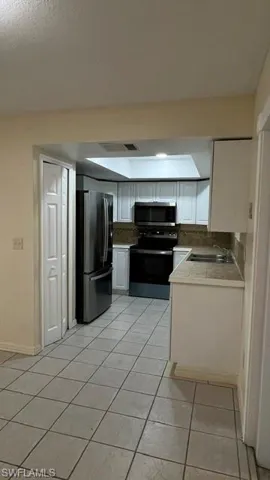 Kitchen featuring white cabinetry, a skylight, tile flooring, and a stainless steel refrigerator