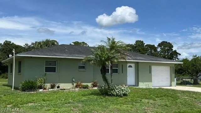 Single-story residence featuring a light green stucco exterior, dark shingle roof, and an attached garage with a white door