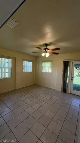 Spacious room featuring neutral-toned tile flooring, multiple windows with blinds, a ceiling fan with integrated lighting, and a glass-paned exterior door