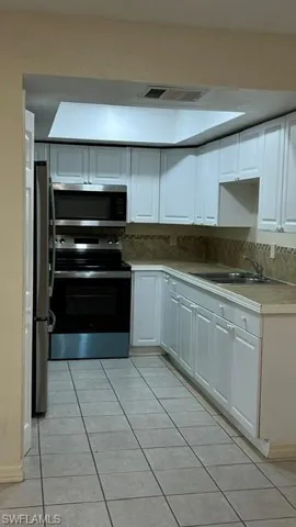 Kitchen featuring white cabinetry, stainless steel appliances, a tile backsplash, and a skylight