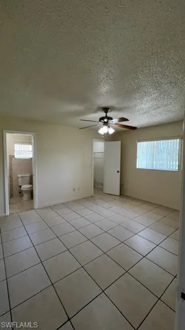 Expansive interior room featuring light-toned tile flooring throughout, a ceiling fan with integrated lighting, and multiple windows with horizontal blinds