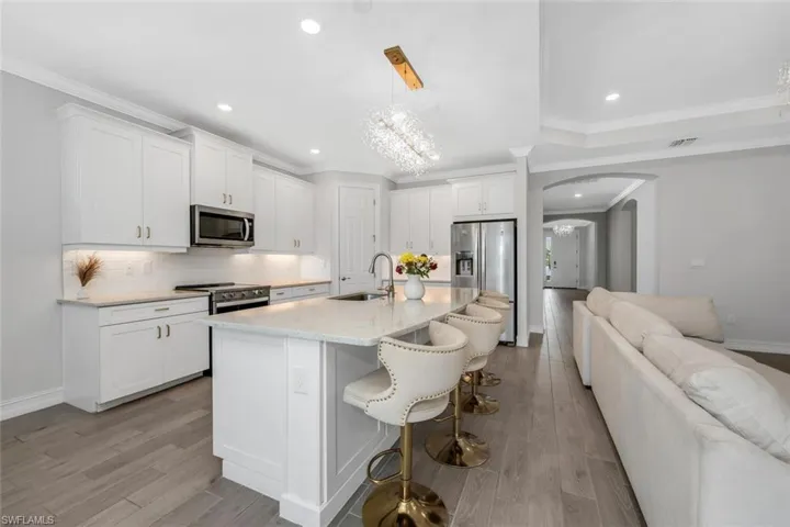 Kitchen featuring arched walkways, suspended lighting, backsplash, stainless steel appliances, and crown molding