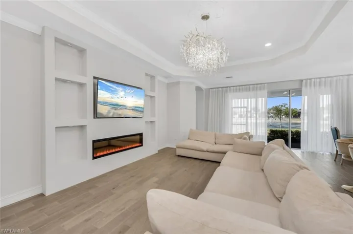 Living room with built in shelves, wood finished floors, hanging lights, crown molding, and a glass covered fireplace