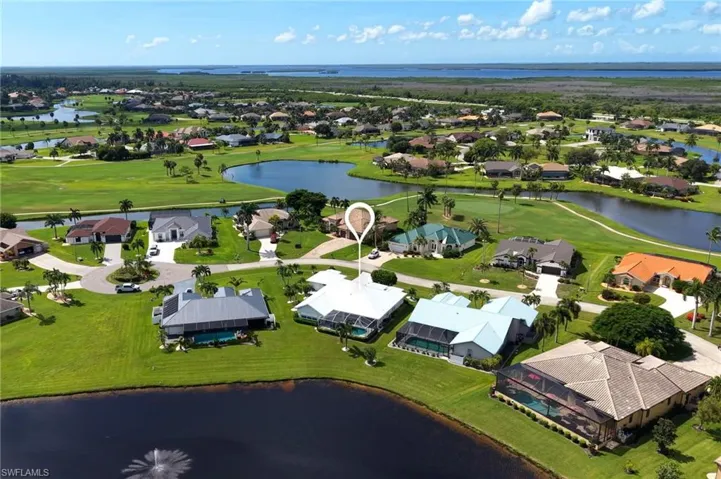 Aerial view of a residential community featuring multiple golf course fairways, interconnected waterways, and a distant body of water