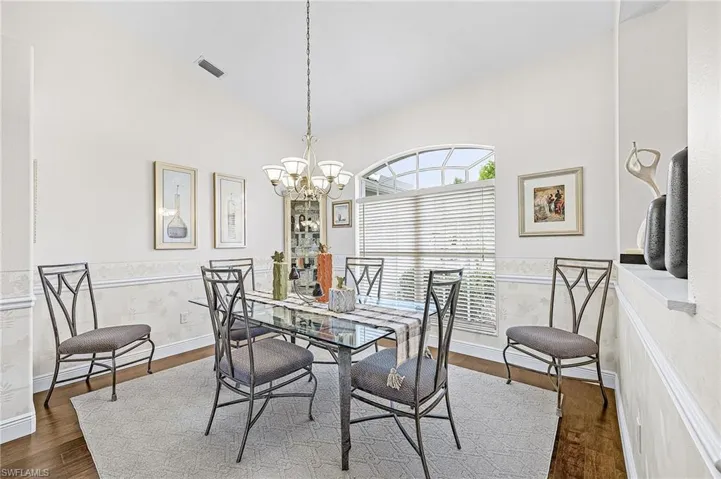 Vaulted ceiling, decorative wainscoting, wood-finish flooring, arched transom window, and a multi-bulb chandelier