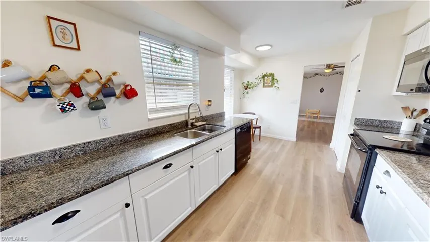 Kitchen with white cabinetry, sink, dark stone counters, black appliances, and light wood-type flooring