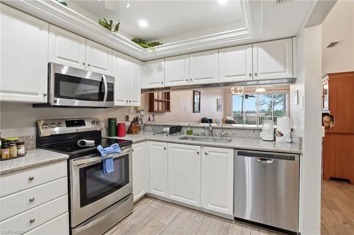 Kitchen with stainless steel appliances, white cabinetry, light wood-style flooring, light stone counters, and ceiling fan