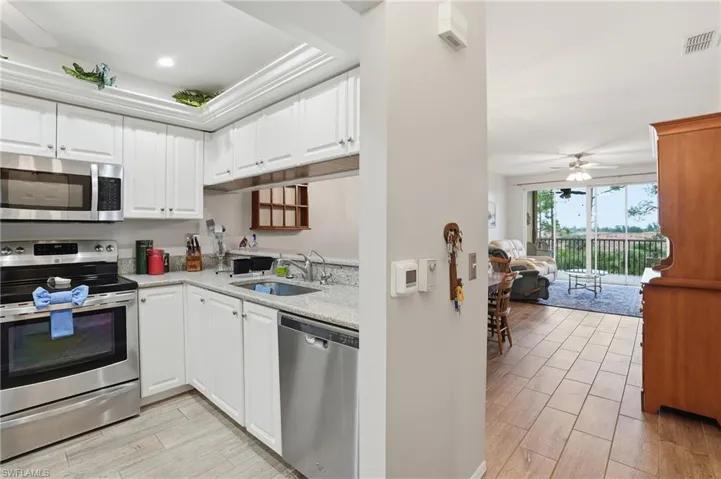 Kitchen with stainless steel appliances, white cabinets, a ceiling fan, light stone counters, and wood tiled floors