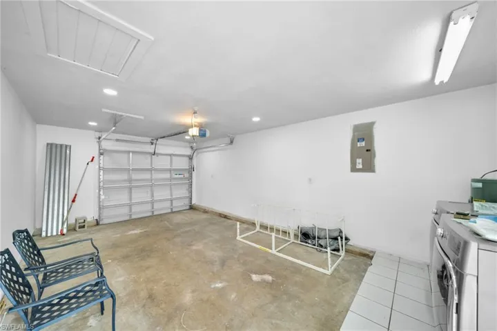 Garage featuring electric panel, washing machine and clothes dryer, a garage door opener, and recessed lighting
