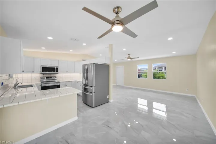 Kitchen with appliances with stainless steel finishes, decorative backsplash, tile countertops, a ceiling fan, and a peninsula