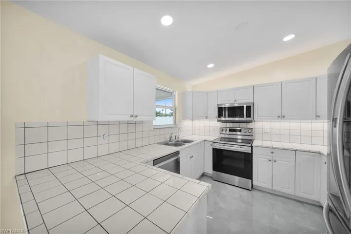 Kitchen featuring stainless steel appliances, vaulted ceiling, decorative backsplash, tile counters, and light marble finish floors