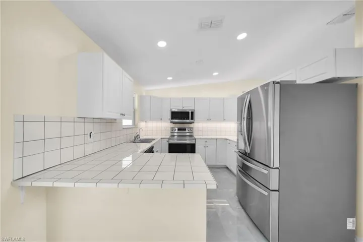 Kitchen with stainless steel appliances, backsplash, a peninsula, tile countertops, and white cabinetry