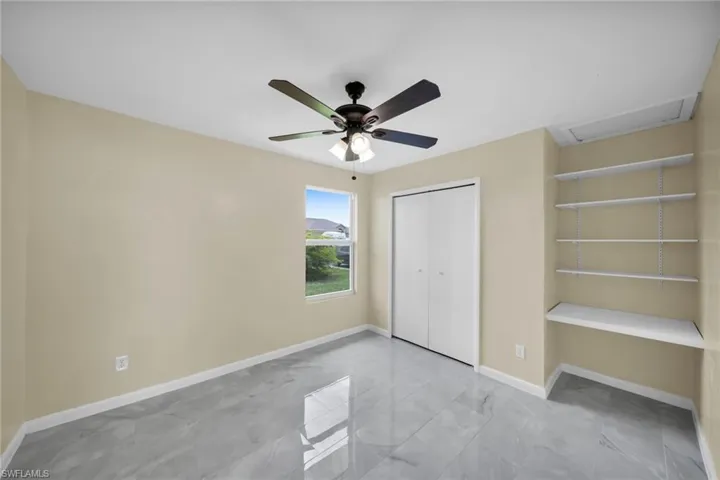 Unfurnished bedroom with attic access, marble look tile flooring, a closet, and a ceiling fan