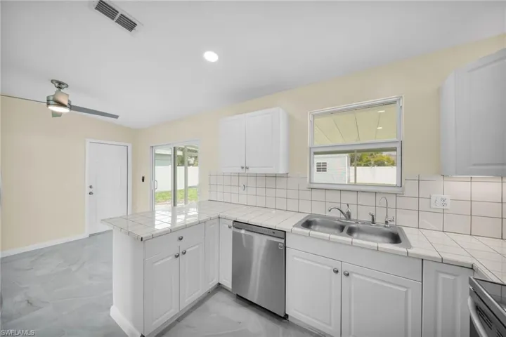 Kitchen with stainless steel appliances, a peninsula, light marble finish flooring, tile countertops, and white cabinets