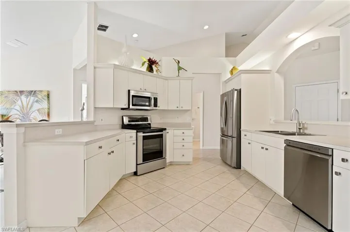 Kitchen featuring vaulted ceilings, white cabinetry, stainless steel appliances, and tile flooring