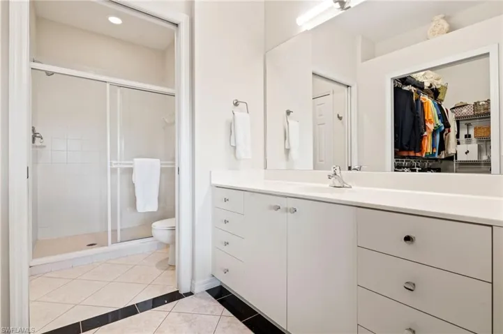 Bathroom featuring a white vanity with extensive storage, a large mirror, and a shower enclosure with sliding glass doors